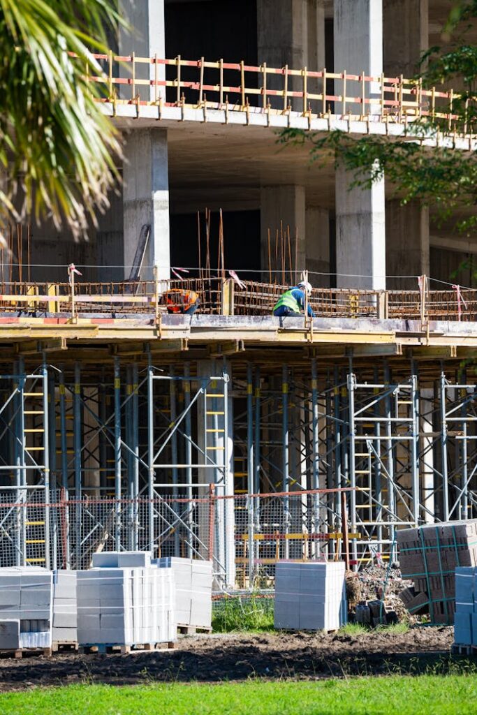 Construction workers on site with scaffolding and materials in sunlight.