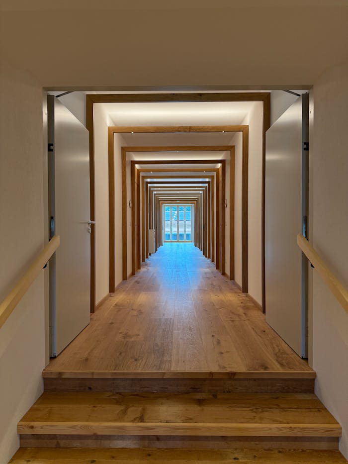 Symmetrical wooden corridor with doors, leading to a distant open door, showcasing minimalist design.