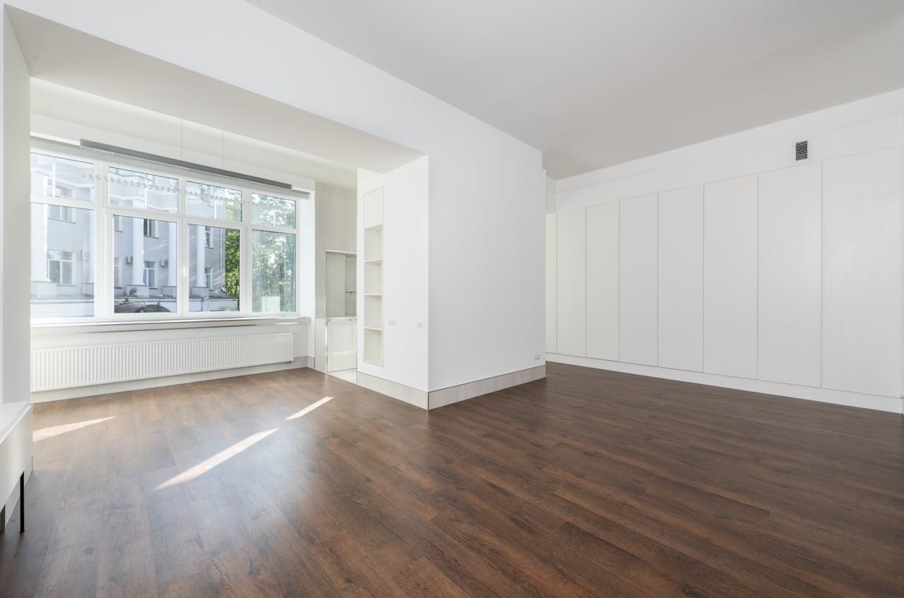 About Bright empty room featuring large windows and wooden flooring.